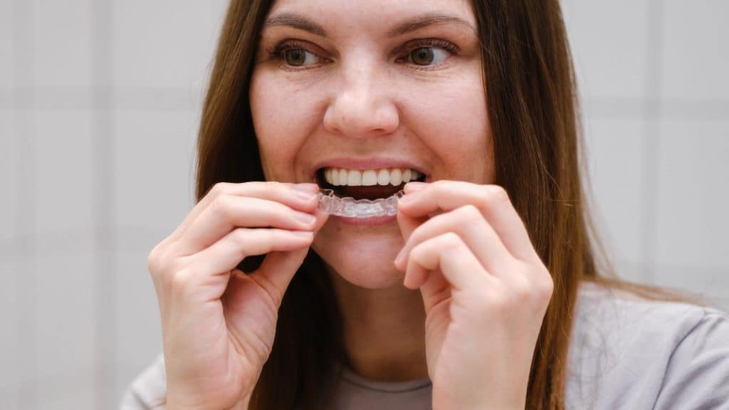 invisalign tedavisi olan bir kadın aynanın önünce şeffaf plak takıyor
