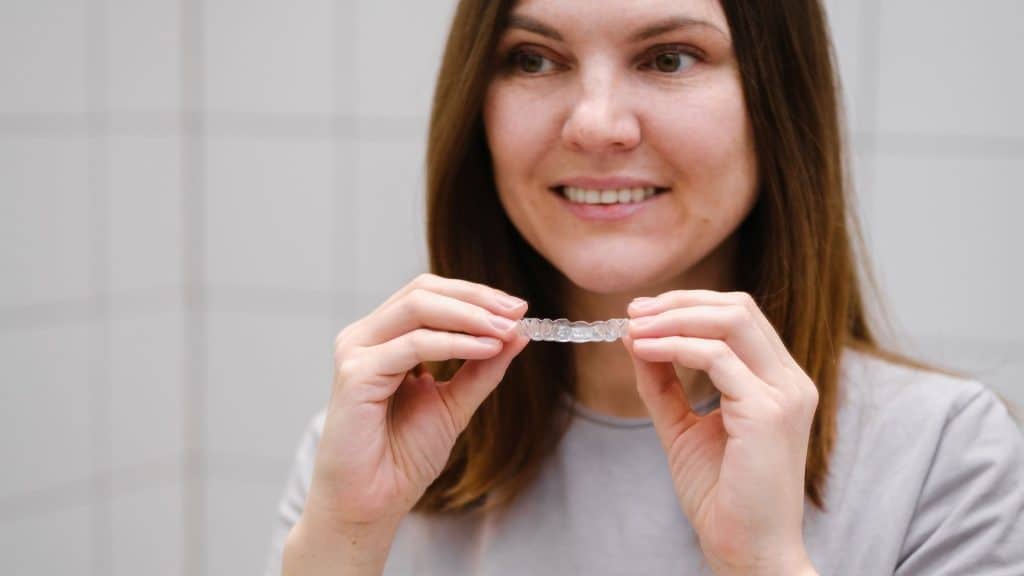 invisalign tedavisi olan bir kadın aynanın önünce şeffaf plak tutuyor