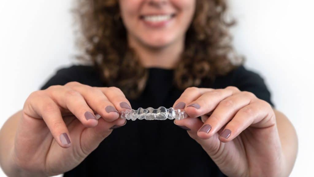 invisalign tedavisi olan bir kadın elinde plak tutuyor